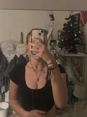 Svart croppad topp från Divided - Säljer en svart croppad topp från Divided med korta ärmar och knappar framtill. Toppen har en  v-ringning och är i ett stretchigt, mjukt matrial.