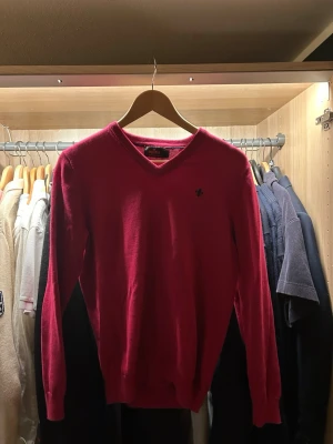 Vinröd ulltröja från Morris - Säljer en vinröd tröja från Morris i 100% ull. Klassisk v-ringad modell med lång ärm och diskret logga broderad på bröstet. Perfekt för dig som gillar stilrena plagg med en färg som sticker ut.