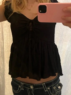 Svart blus med knyt från 157 - Supersöt svart blus från 157 i storlek XS. Modellen har korta ärmar, v-ringning och knyt framtill som ger en fin detalj! 💗