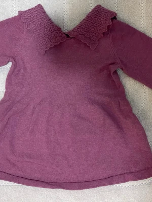 Stickad lila klänning med krage - Säljer en söt stickad lila klänning med långärmad design och en bred, dekorativ krage med mönstrad stickning. Perfekt för dig som gillar mjuka material och vill ha något som sticker ut med sin fina krage.