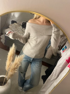Beige offshoulder stickad tröja - Säljer en beige stickad tröja med bred ribbad kant som sitter snyggt offshoulder. Tröjan har lång ärm och är mjuk i materialet, perfekt för dig som gillar en chill och stilren look. Passar till jeans eller kjol och har en neutral ton som är lätt att matcha.