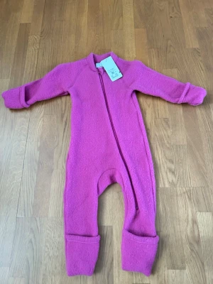 Rosa ulloverall  - Mysig rosa overall från Cubus i 100% merino. Overallen har dragkedja framtill som går snett över kroppen och vikbara muddar vid ärmar och ben. Perfekt för kyliga dagar och enkel att ta på och av.