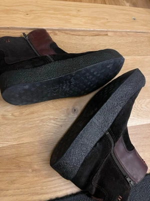 Svarta vinterboots från Canada Snow - Säljer ett par svarta vinterboots från Canada Snow med bruna detaljer i skinn och mjukt grått foder. Skorna har dragkedja på sidan och en robust, platt sula som ger bra grepp. Utsidan är i mocka och insidan är fodrad med päls för extra värme.