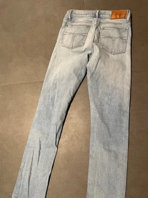 Ljusblå jeans från Tiger of Sweden - Säljer ett par ljusblå jeans från Tiger of Sweden med klassisk femficksdesign och raka ben. Jeansen har snygga kontrastsömmar, normal passform och är tillverkade i mjukt bomullsjeansmaterial. Perfekta för dig som gillar stilrena och tidlösa jeans.