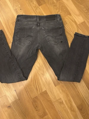 Grå slimfit jeans storlek 27/30 - Säljer ett par gråa slimfit jeans med snygg tvätt och klassiska fem fickor. Jeansen har smal passform och normal midja, perfekta för dig som gillar en stilren look. Materialet är mjukt jeans och färgen är mörkgrå med lätt slitning.
