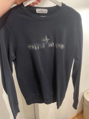  Stone Island sweatshirt - Svart sweatshirt från Stone Island med diskret logotyp tryckt på bröstet och en liten rund logga i nacken. Tröjan har rund hals och långa ärmar, tillverkad i mjuk bomull som är skön att ha på sig. Den är helt äkta.