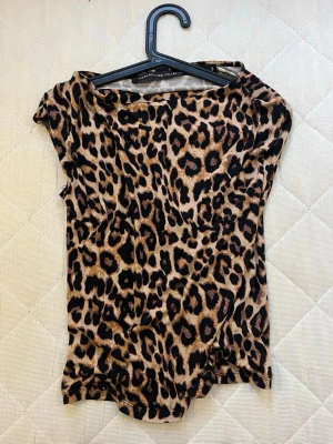 Leopardmönstrad topp från Black Label - Säljer en snygg leopardmönstrad topp från Black Label Collection i storlek S. Toppen har korta ärmar och är gjord i ett mjukt, stretchigt syntetmaterial. Perfekt för dig som gillar djurmönster och vill sticka ut med en cool look.