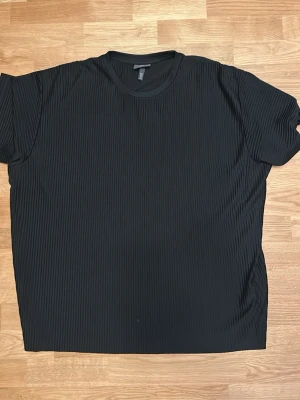 Svart ribbad t-shirt från H&M XL - Säljer en svart t-shirt från H&M i loose fit med ribbad struktur. T-shirten har korta ärmar och rund halsringning, perfekt för dig som gillar en chill och enkel stil. Materialet känns mjukt och följsamt mot kroppen.