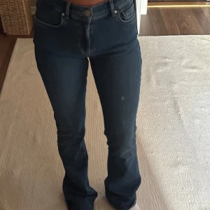 Blå low flare jeans med låg midja - Säljer ett par blå jeans med låg midja och flare-ben. Jeansen har klassisk femficksdesign, dragkedja och knapp framtill. Materialet är jeans i bomull och de har en snygg, mörkblå tvätt. Perfekta för dig som gillar en trendig och avslappnad look. Mycket stretch!! Passar längd 160-165 cm