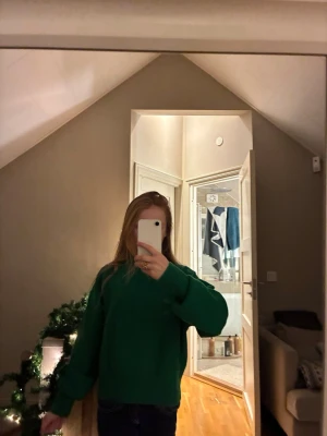 Grön stickad tröja med hög krage - Säljer en grön stickad tröja med hög krage och långa ärmar. Tröjan har en loose passform och breda muddar vid ärmslut och nederkant. Perfekt för kyliga dagar och enkel att styla med jeans eller kjol.