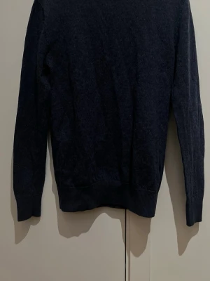 Mörkblå merinoulltröja John Henric - Säljer en stilren mörkblå tröja från John Henric i storlek S men känns mer som XS. Tröjan är stickad i 100% merinoull och har rund hals samt ribbade muddar vid ärmslut och nederkant. Perfekt för dig som gillar klassisk och enkel design.