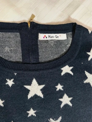 Mörkblå stickad tröja med stjärnor S - Snygg mörkblå stickad tröja från Man Ge med vita stjärnor över hela plagget. Tröjan har rund hals och en dragkedja i ryggen som cool detalj. Ribbstickade muddar vid ärmslut och nederkant. Perfekt för dig som gillar unika mönster och vill sticka ut.
