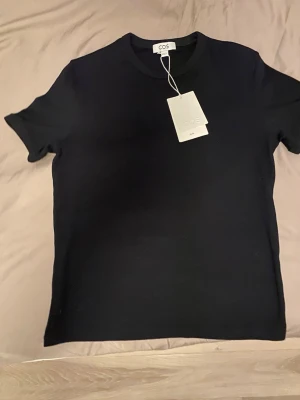 Cos ribbad tee - Figurnära ribbad T-shirt i bomull från cos i svart. Helt ny, aldrig använd då den är för liten för mig. Storlek M. Nypris är 390kr