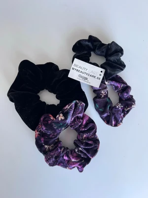 4-pack scrunchies i sammet (nya) - 4st scrunchies. Två minde och två större. Lila med blommor och helsvarta. De små är oanvända med prislapp kvar och de större är testade. Säljer pga att jag inte använder scrunchies längre. - Köper du innan kl 16:00 kan jag posta samma dag!