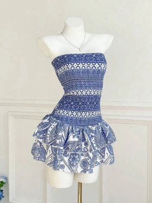 Blåvit axelbandslös kortklänning - Superfin blåvit axelbandslös kortklänning med smockad överdel och volangig kjol. Klänningen har ett snyggt paisleymönster och sitter tight upptill. Perfekt för varma dagar och ger en fräsch sommarkänsla!
