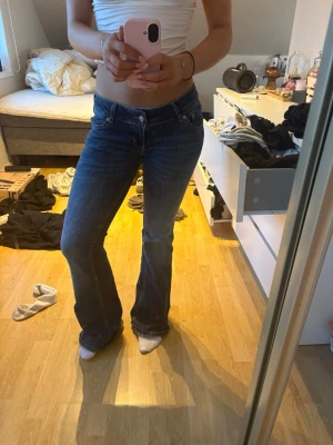 Blå bootcut jeans lågmidjade - Säljer ett par klassiska blå jeans med bootcut-modell och låg midja. Jeansen har fem fickor, snygga sömmar och är tillverkade i ett mjukt denimtyg. Perfekta för dig som gillar en retro vibe och vill ha ett par jeans som sitter snyggt över höfterna.