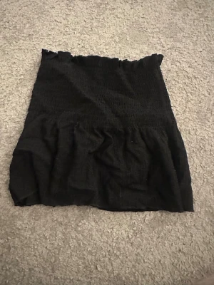 Svart smockad linnetopp med volang - Svart linnetopp med smockad överdel och volang nedtill. Toppen har tunna, justerbara axelband och är tillverkad i ett mjukt tyg som ger en skön känsla. Perfekt för sommarens varma dagar och enkel att matcha med jeans eller kjol.