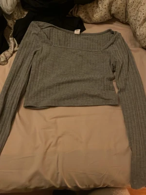 Grå ribbad top långarmad  - Säljer en grå croppad topp med ribbad struktur och offshoulder-design. Toppen har långa ärmar och är perfekt för dig som gillar en stilren och enkel look. Materialet känns mjukt och stretchigt, vilket gör den bekväm att bära.