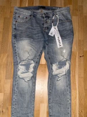 Blå ripped jeans från Purple Brand - Säljer ett par blå jeans från Purple Brand med snygga slitningar och stora hål på knäna. Jeansen har fem fickor, klassisk passform och är tillverkade i jeansmaterial. De har en ljus tvätt och coolt distressed utseende som ger en trendig vibe. Pris kan diskuteras 