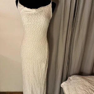 Vit spetsklänning från Bershka - Supersnygg lång vit klänning från Bershka med smala axelband och spetsmönster över hela klänningen. Den har en figurnära passform och är perfekt för dig som vill ha en elegant och stilren look. Klänningen är fodrad och känns riktigt lyxig.
