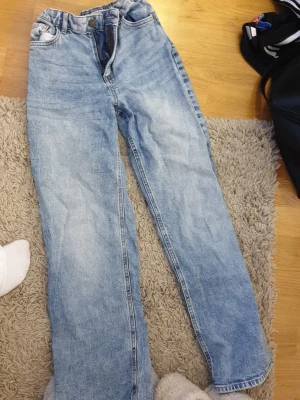 Blå raka jeans från Lindex - Snygga ljusblå jeans från Lindex med klassisk femficksdesign och raka ben. Jeansen har normal passform och är tillverkade i mjukt bomullsmaterial med en lätt tvättad look. Perfekta för dig som gillar enkel och stilren denim.