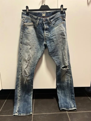 Ljusblå Vintage Replay jeans med ljus tvätt och slitningar - Säljer ett par klassiska Vintage replay i ljusblå tvätt med slitna detaljer och hål på benen. Storlek 31/32. bra skick! pris kan diskuteras vid snabb affär
