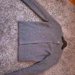 Grå kofta från Zara med knapp - Mysig grå kofta från Zara i storlek S. Koftan har en enkel design med rund halsringning och en stor knapp framtill. Tillverkad i mjukt material som känns skönt mot huden och har långa ärmar. Perfekt att slänga på sig när det är lite kyligare ute. Lite cardigan aktig