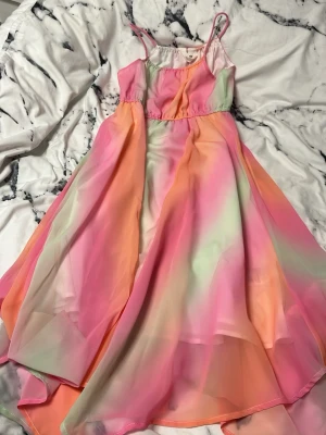 Färgglad långklänning från H&M - Säljer en superfin långklänning från H&M med tunna axelband och ett flowigt tyg. Klänningen har ett mjukt färgskiftande mönster i rosa, orange och ljusgrönt, vilket ger en dreamy vibe. Materialet är lätt och känns som syntet, perfekt för varma dagar.