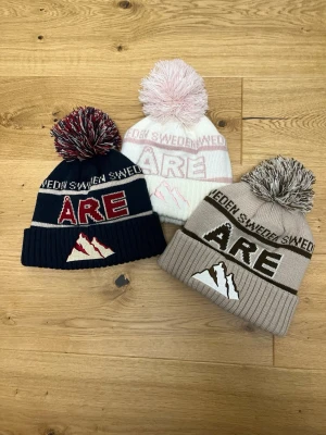 Åre Mössor - Riktigt stiliga och trendiga mössor som även onewear har gjort en version av. De här är de originella från Robin Root (köpta i åre). Bilden visar tre stickade mössor med texten Åre och Sverige, samt bergs motiv. 370 st eller 1100 för alla tre