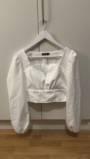 Vit croppad blus från SHEIN - Säljer en vit croppad blus från SHEIN i storlek S. Blusen har långa puffärmar, fyrkantig urringning och snygga veckade detaljer framtill. Materialet är glansigt och känns lyxigt, perfekt för att sticka ut. Dragkedja i ryggen för enkel påklädning.