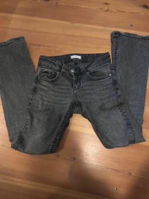 Bootcut lowwaist jeans mörkgrå - Säljer ett par snygga utsvängda och lågmidjade jeans. De har coola knappar på bakfickorna. Strl 34. Säljer pga att de inte kommer till användning längre.  Skriv om du har frågor!☺️