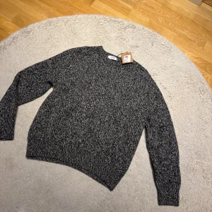 Mörkgrå stickad tröja från COS - Säljer en mörkgrå stickad tröja från COS med melerad look. Tröjan har rund hals, långärmade ärmar och en loose passform som ger en chill vibe. Perfekt för dig som gillar minimalistisk stil och vill ha något som funkar hela hösten och vintern.