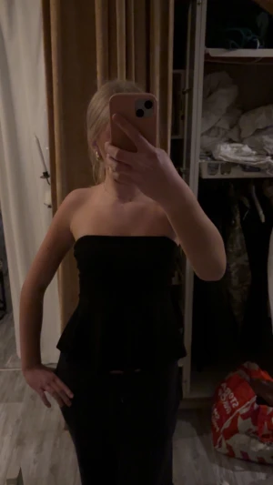 Svart bandeau tubtopp med volang - Säljer en svart bandeau tubtopp med volang nertill. Toppen är axelbandslös och har en figurnära passform upptill som släpper ut i en lätt volang. 