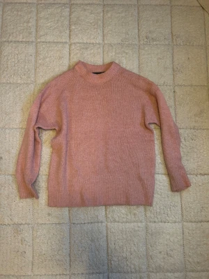 Rosa stickad tröja från 157 - Mysig rosa stickad tröja från 157 med rund halsringning och ribbade muddar. Perfekt för lager på lager under höst och vinter. Tröjan har en relaxed passform och är superenkel att styla till jeans eller kjol.