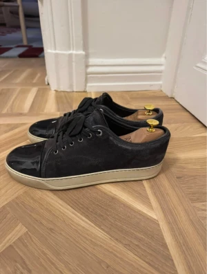 Gråa lanvin skor - Snygga gråa  sneakers från Lanvin med ovandel i mocka och lackad tå. Skorna har svarta snören, silverfärgade öljetter och en beige platt sula. Perfekta för dig som gillar stilrena och exklusiva detaljer. Klassisk rund tå och diskret branding på sulan. Uk9