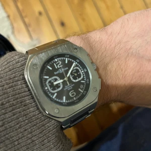 Bell & Ross kvadratisk kronografklocka - Stilren kvadratisk klocka med svart urtavla, silverfärgade visare och index samt två subdials. Boetten och länken är i borstat stål och klockan har tydliga skruvar i hörnen för en industriell look. Perfekt accessoar för dig som gillar modern design.  Har fått de  och kommer därför INTE med låda mm, länkarna är utbytta och finns extra om man vill ha större. Priset är tillfälligt, säljer eller byter med annan klocka.