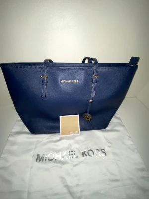 Michael Kors Jet Set Tote – blå saffianoläderväska i toppskick - Stilren och rymlig Michael Kors toteväska i blått saffianoläder. Perfekt som vardagsväska, jobbväska eller shoppingbag. Har dubbla axelremmar, MK-logotyp i guld och klassisk struktur i lädret. Levereras med original dustbag och tagg.