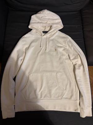 Vit hoodie från Polo Ralph Lauren - Snygg vit hoodie från Polo Ralph Lauren i storlek M. Tröjan har huva med snörning, klassisk känguruficka och det ikoniska Polo-logot broderat på bröstet. Tillverkad i mjuk bomull, perfekt för chill dagar. Långärmad och med ribbade muddar för extra komfort.