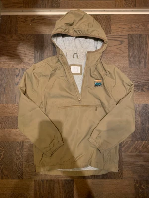 Beige vindjacka med huva från Zara - Snygg beige vindjacka från Zara med huva och halv dragkedja framtill. Jackan har en praktisk ficka med dragkedja på bröstet och ett litet färgglatt märke. Den har även dragkedja på vardera sida av jackan. Insidan är fodrad i grått tyg och ärmarna har resår vid mudden. Perfekt för blåsiga dagar. Vid frågor, hör av dig! 