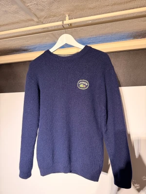 Lacoste ull tröja - Riktigt fin tjock ull tröja från Lacoste i en marinblå färg. Väldigt fint skick utan några defekter. Är lite liten i storleken så passar XS/S skulle jag säga, har själv normalt S