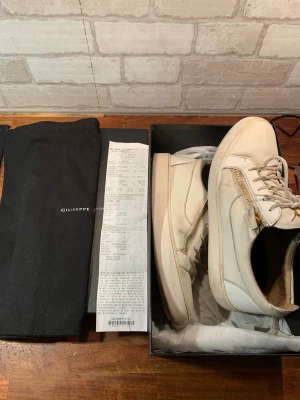 Giuseppe Zanotti - Snygga vita sneakers från Giuseppe Zanotti i skinn med guldfärgade dragkedjor.                                         Köpt på NK så kvitto och box o allt finns!!!!                Skick 7/10( använda väl men har mycket kvar o ge).      Storlek 45. Pris 1899kr!!