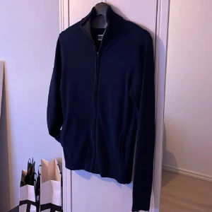 Mörkblå ziptröja från Pier One - Mörkblå tröja med dragkedja från Pier One. Tröjan har hög krage med grå insida och ribbade muddar vid ärmslut och nederkant. Perfekt för lager-på-lager och enkel att matcha med olika outfits.