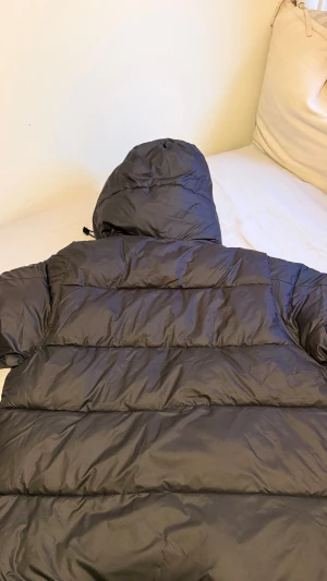 Svart pufferjacka från Burberry - Svart pufferjacka från Burberry med huva och klassiskt rutigt foder i grått och vitt. Storleken passar L och XL den är väldigt skön och varm så den passar vädret på vintern. Den kan också bli till en väst genom att dra bort kedjorna inneifrån jackan så de blir en väst och den passar för våren, sommaren och hösten. För mer information kontakta mig. Den är helt oanvänd har bara testat den själv och den passade inte mig och därför säljer jag den.