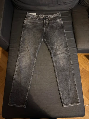 Slim fit svarta jeans från H&M - Slim fit jeans från H&M i tvättad svart färg med klassisk femficksdesign. Jeansen har smal passform och raka ben, tillverkade i jeansmaterial med snyggt slitna detaljer. Perfekt för dig som gillar en stilren och modern look.