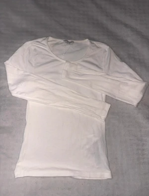 Vit långärmad tröja i bomull - En enkel och stilren vit långärmad tröja med rund hals. Tröjan är figurnära och tillverkad i mjuk bomull, perfekt för lager-på-lager eller att bära som den är. Passar dig som gillar clean och minimalistisk stil.