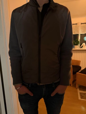 Grå cardigan från Massimo Dutti - Snygg grå cardigan från Massimo Dutti med stilren design och hel dragkedja framtill. Jackan har slät framsida och baksida, samt stickade ärmar i mörkgrå ton. Perfekt för dig som gillar en clean look och vill ha något lätt och bekvämt.