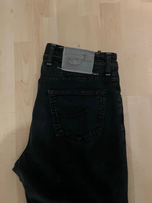 Svarta Jacob Cohen jeans 688 Comfort - Svarta jeans från Jacob Cohen med klassisk femficksdesign och silverfärgade knappar. Modellen är 688 Comfort med rak passform och snygga detaljer som broderad J på myntfickan och grå patch bak. Jeansen är tillverkade i mjukt bomullstyg för extra komfort.