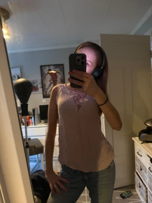 Ljusrosa blus med spets från ONLY - Säljer en ljusrosa blus från ONLY i storlek 38. Toppen är ärmlös och har en snygg spetsdetalj med blommönster framtill vid halsen. Materialet är mjukt och lätt, perfekt för varmare dagar. Passformen är normal och toppen är enkel att matcha med jeans eller kjol.