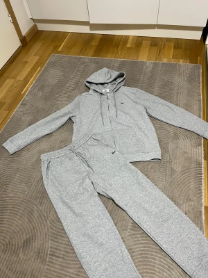 Lacoste tracksuit - En fin Lacoste tracksuit i grå. Storlek M samt så är den unisex. Om du är intresserad,så kan du lägga ett bud