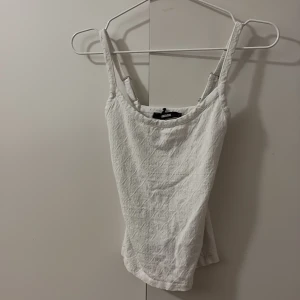 Vit broderad linnetopp från Bik Bok - Supersöt vit linnetopp från Bik Bok med broderade detaljer och justerbara axelband. Toppen har ett diskret blommönster i tyget och är perfekt för varma dagar. Sitter snyggt och är lätt att matcha med jeans eller kjol.